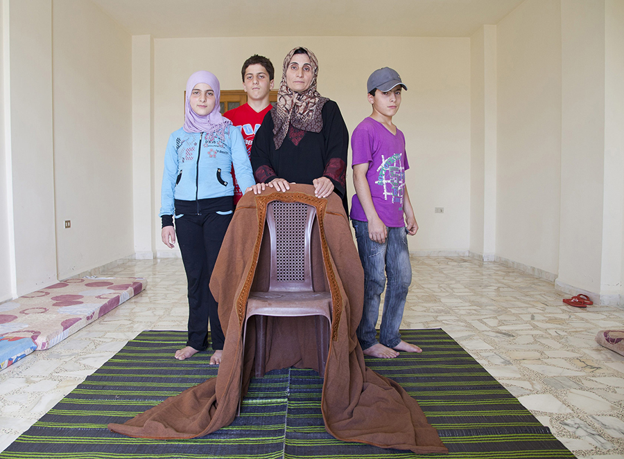 Rahab and her children in their apartment in Qobayat, Lebanon, stand around an empty chair, cloaked with their father’s robe. He was killed when a shell hit their neighbourhood in Homs, Syria. UNHCR / E.Dorfman / September 2013 (Common Licence FLickr)